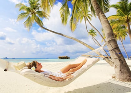 Photo of a young woman relaxing in a hammock that is tied to palm trees on the beach, for information on Hoffman Estates sedation dentistry from Dr. William Becker.