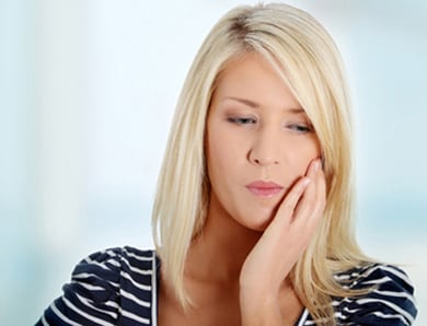 Head-and-shoulders photo of a blonde woman holding the left side of her face with her left hand; for information on toothaches from Dr. Becker of Hoffman Estates.