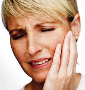 A woman grabbing her jaw in pain from TMJ
