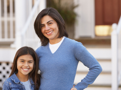 Photo of a brunette mother and 10+ year-old daughter standing outside of a house; for information on family dentistry from Hoffman Estates dentist Dr. William Becker.